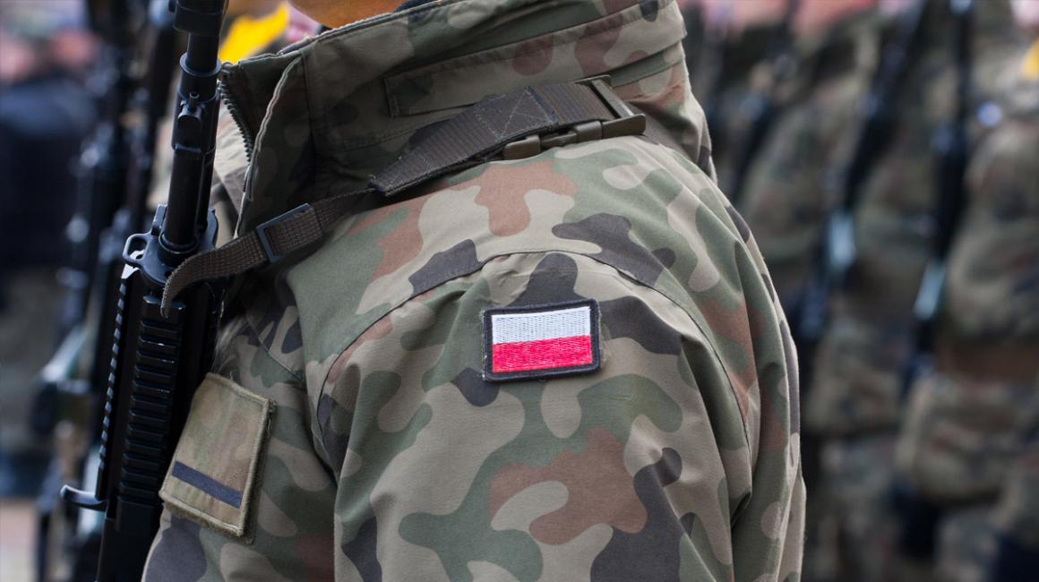 Fragment salutującego żołnierza w mundurze z naszywką w polskich barwach