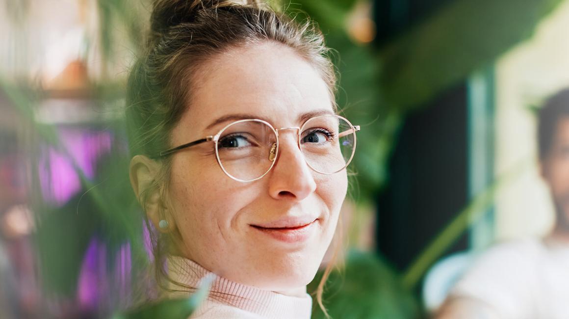 Odwrócona w stroną oglądającego siedzaca kobieta w okularach. Na drugim placie siedzący mężczyzna