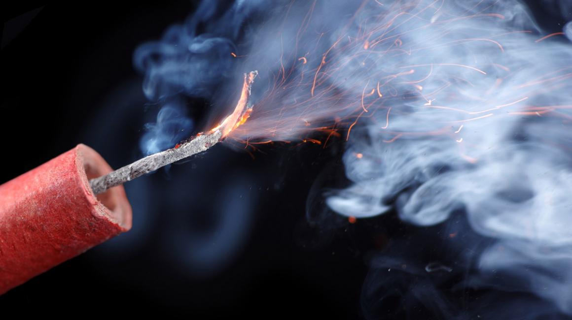 Palący się lont petardy. W tle dużo dymu