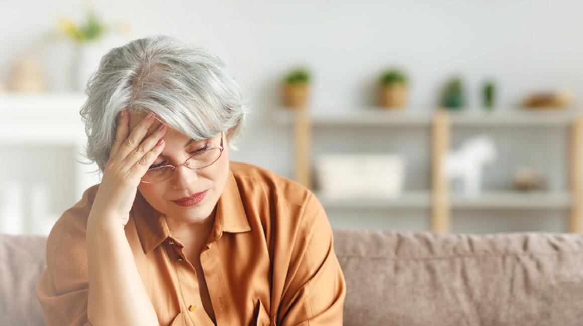 Kobieta na kanapie przed laptopem, podpierająca głowę ręką w geście przytłoczenia