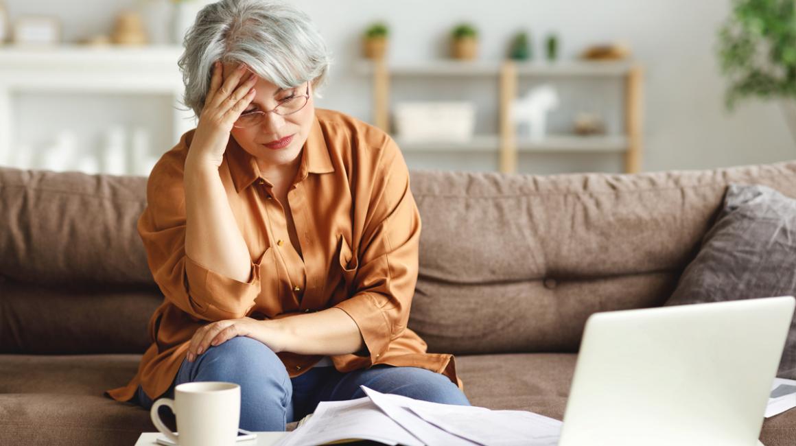 Kobieta na kanapie przed laptopem, podpierająca głowę ręką w geście przytłoczenia