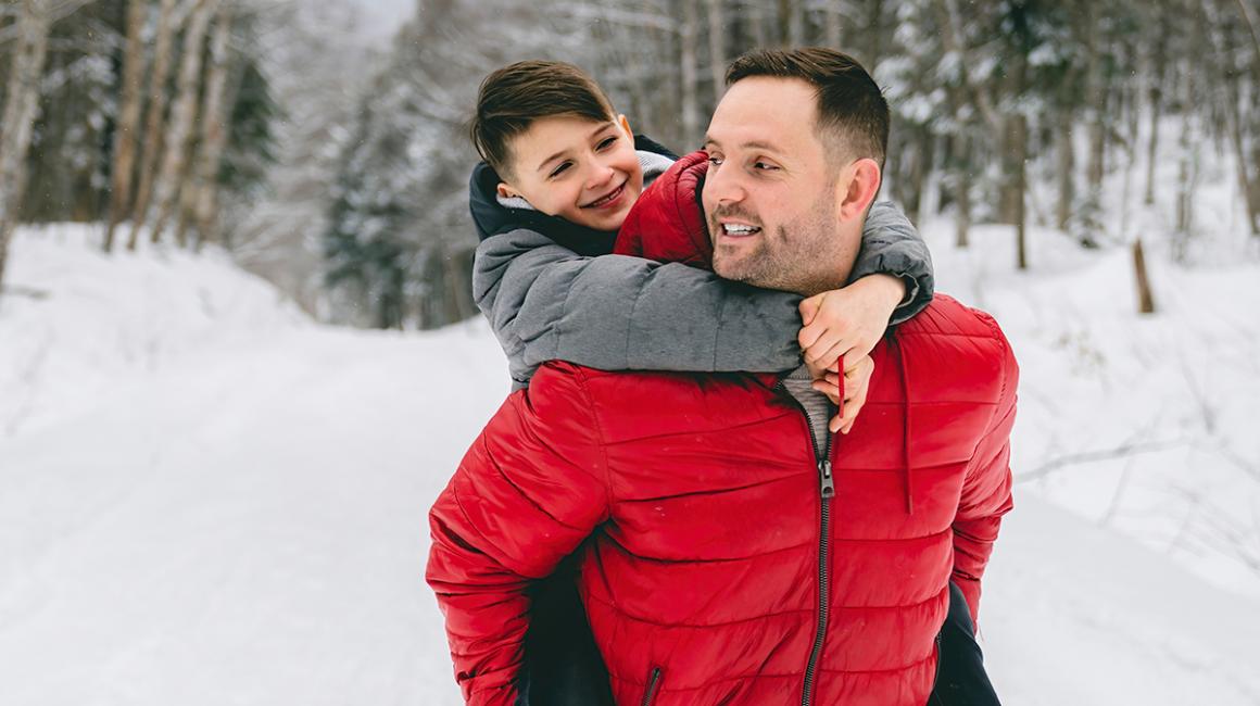 Ojciec niesie syna na barana, są w śnieżnym lesie
