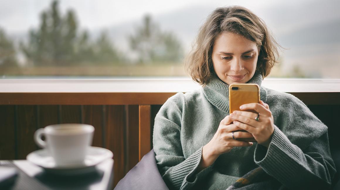 Kobieta w dresie patrzy na komórkę, przed nią kawa