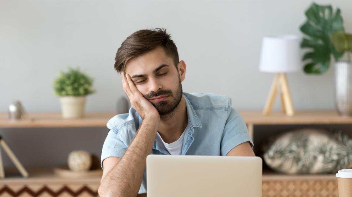 Mężczyczna przed laptopem, głowa podparta na dłoni.
