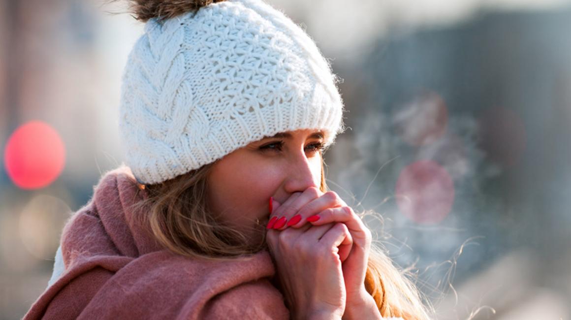 Kobieta w białej czapce, chuchająca w ręce, żeby się rozgrzać