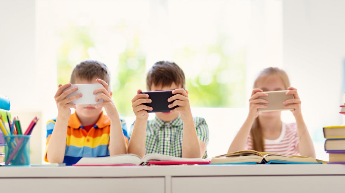 Trójka dzieci przy stole wpatrzonych w w swoje smartfony