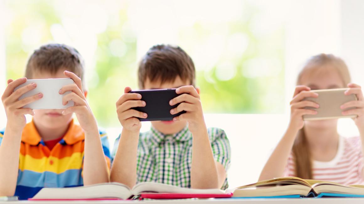 Trójka dzieci przy stole wpatrzonych w w swoje smartfony
