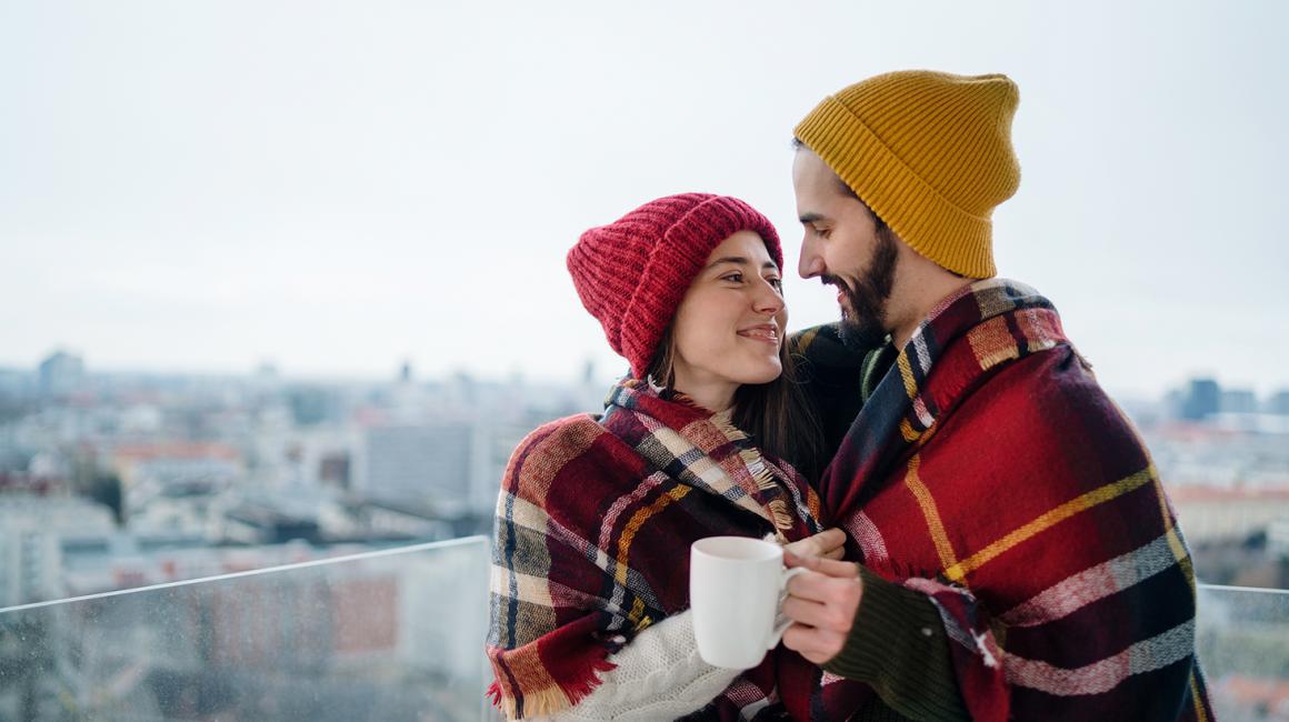 Ona w czerwonej czapce, on w żółtej, na tle mroźnego miasta otulają się kocem