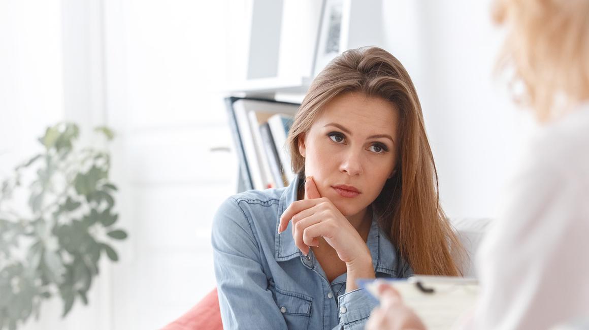 Na pierwszym planie mamy zadbaną młodą kobietę. Słucha, co mówi druga, która siedzi do nas tyłem.