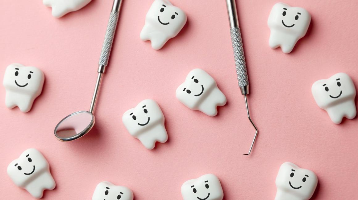 Rozrzucone plastikowe białe zęby z dorysowanymi uśmiechami, a wśród nich narzędzia dentysty - lusterko i hak.