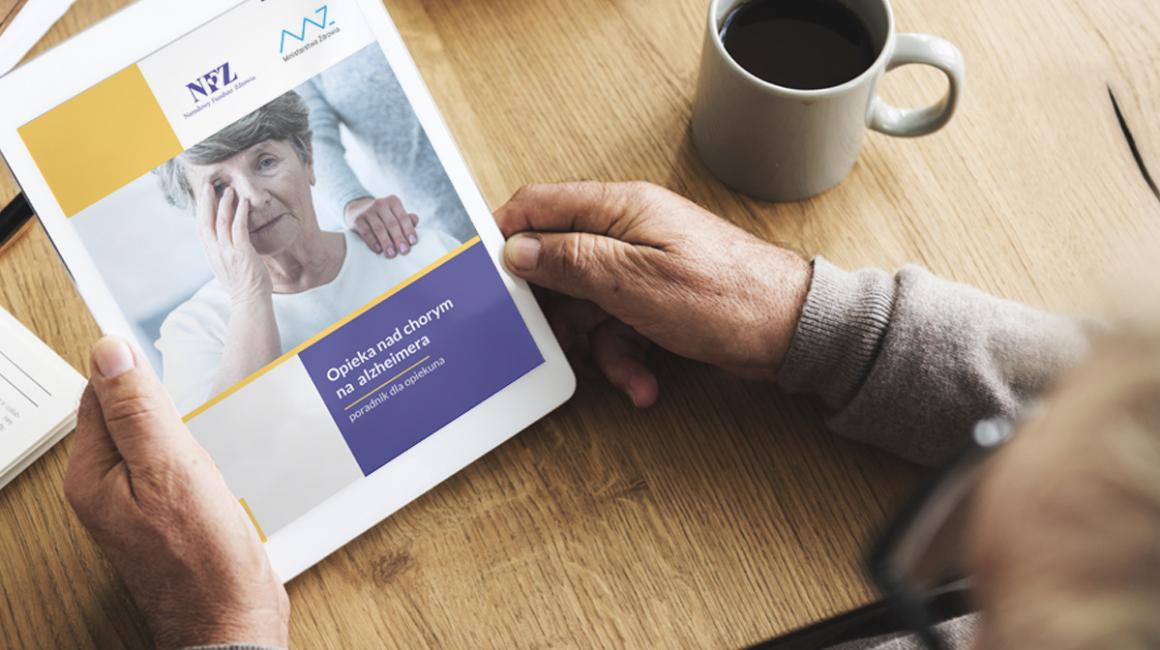 Mężczyzna trzyma w rękach tablet. Ma na nim wyświetlony poradnik dla opiekunów nad chorym na alzheimera 