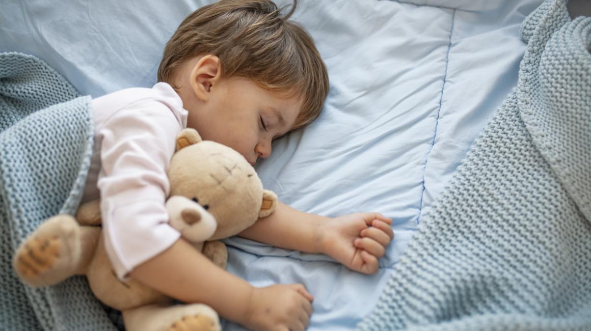 Mały chłopczyk śpi pod kocem. Przytula się do misia.