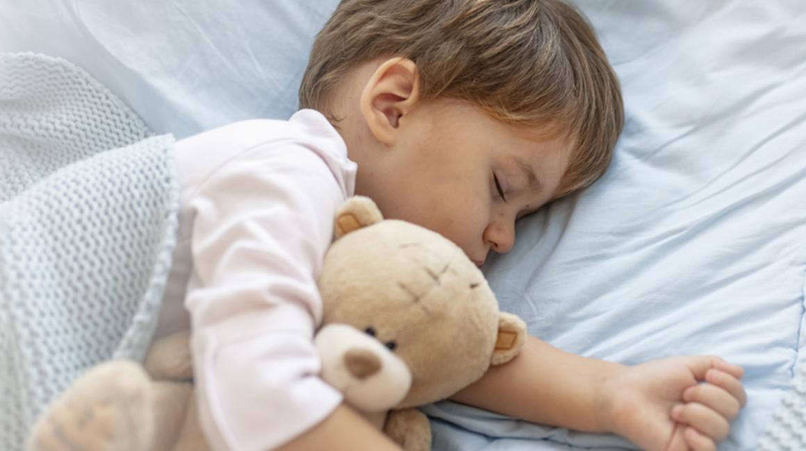 Mały chłopczyk śpi pod kocem. Przytula się do misia.