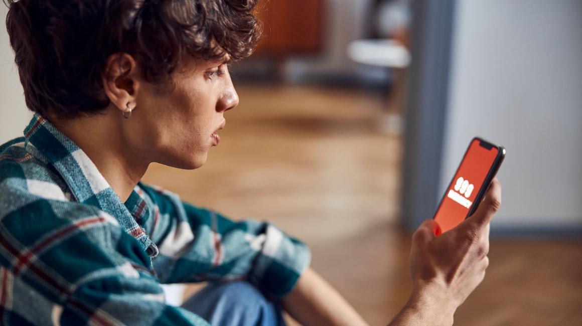 Mlody chłopak trzyma telefon, na którym wyświetla się numer 999. Jest w domu i dzwoni po pomoc.