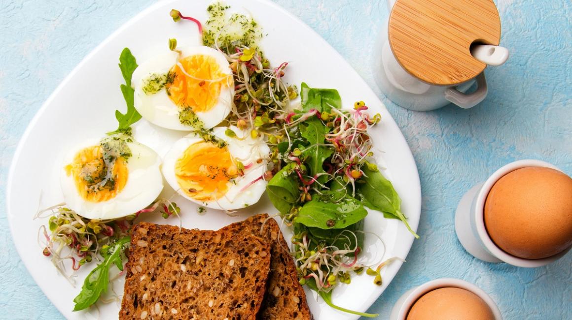 Zdrowe śniadanie. Jajka ugotowane na twardo, świeże kiełki rzodkiewki, rukola z sosem ziołowym i kromki pełnoziarnistego ciemnego chleba.