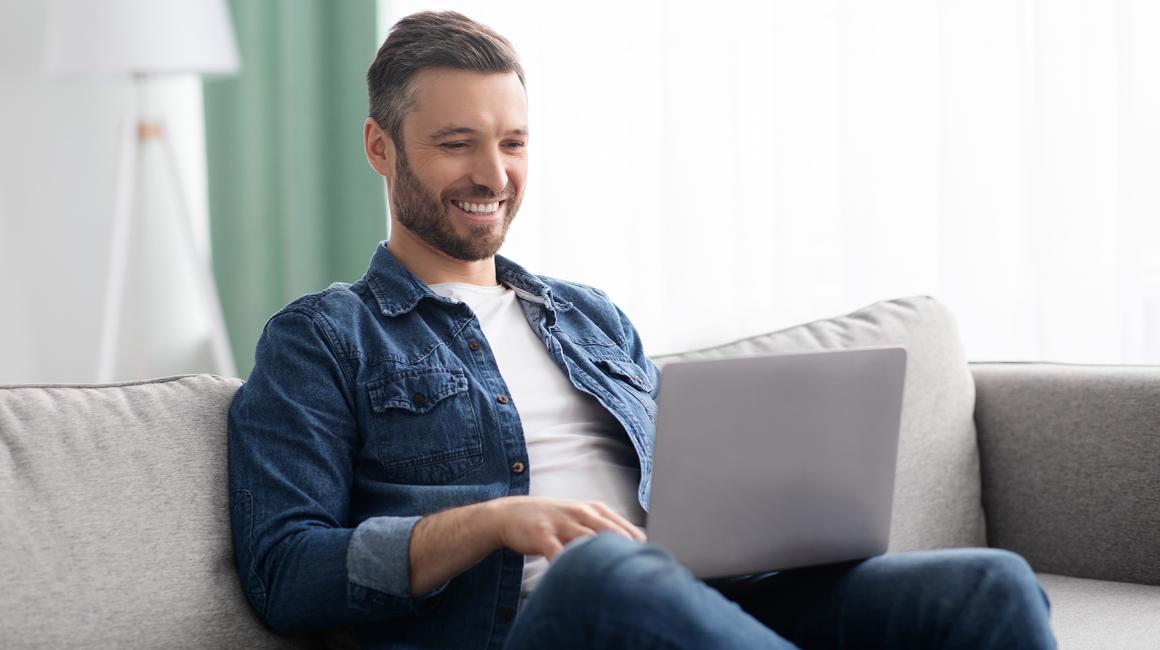 Uśmiechnięty mężczyzna z laptopem na kolanach