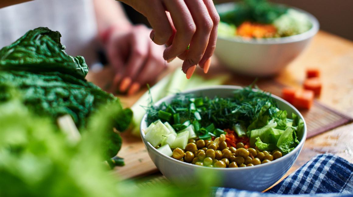 Kobieca ręka posypuje posiekanym koperkiem zielone warzywa w misce.
