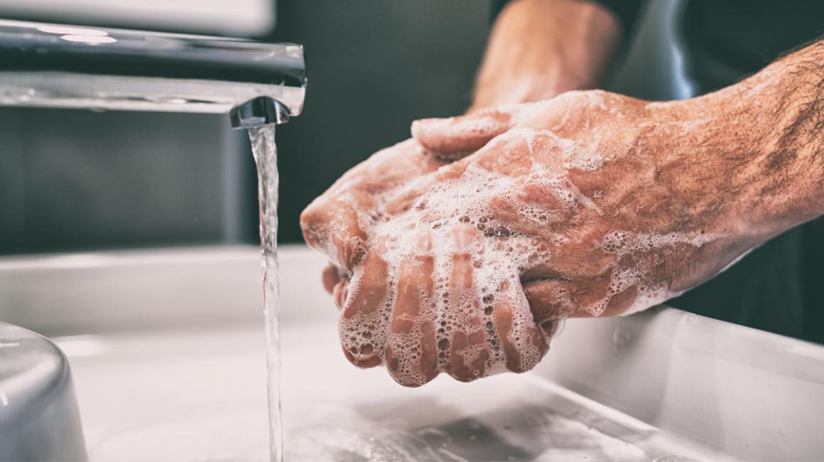 Namydlone dłonie mężczyny nad umywalką podczas mycia rąk.