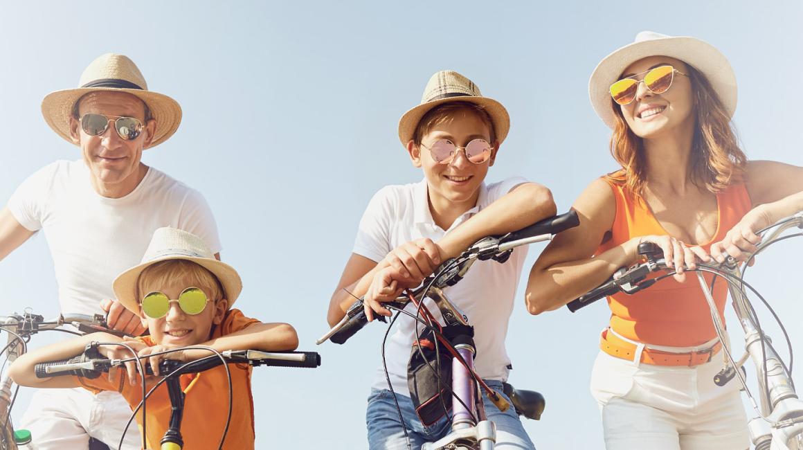 Czteroosobowa rodzina w słoneczny dzień na rowerach. Każda osoba ma kapelusz i okulary przeciwsłoneczne.