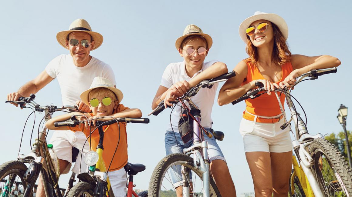 Czteroosobowa rodzina w słoneczny dzień na rowerach. Każda osoba ma kapelusz i okulary przeciwsłoneczne.