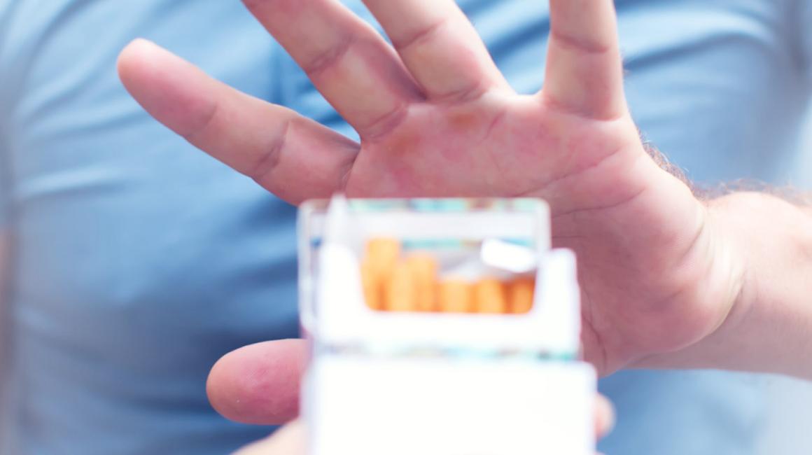 Mężczyzna gestem unisionej dłoni odmawia wzięcia papierosa z pełnej paczki.