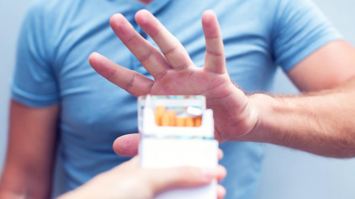 Mężczyzna gestem unisionej dłoni odmawia wzięcia papierosa z pełnej paczki.