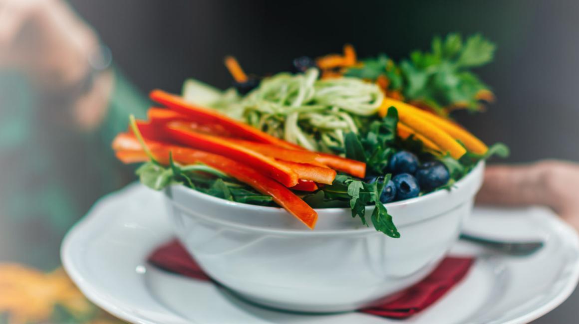 Kelner podaj danie na talerzu. Jest na nim papryka, marchewka, borówka amerykańska, pieruszka, zielony makaron.