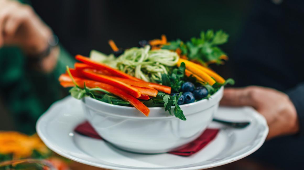 Kelner podaj danie na talerzu. Jest na nim papryka, marchewka, borówka amerykańska, pieruszka, zielony makaron.