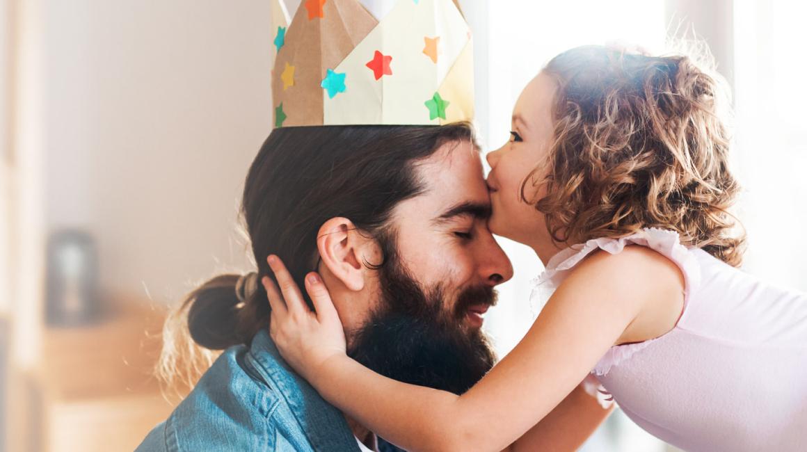 Córeczka w stroju baletnicy całuje ojca w czoło. Mężczyzna ma na głowie papierową koronę.