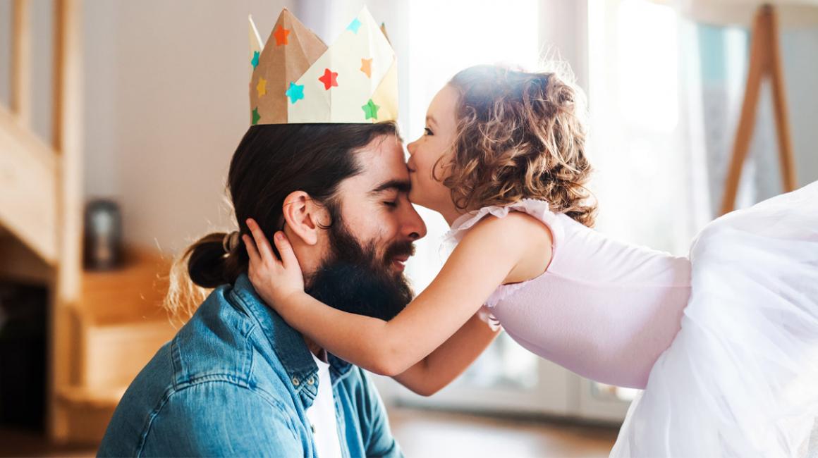 Córeczka w stroju baletnicy całuje ojca w czoło. Mężczyzna ma na głowie papierową koronę.