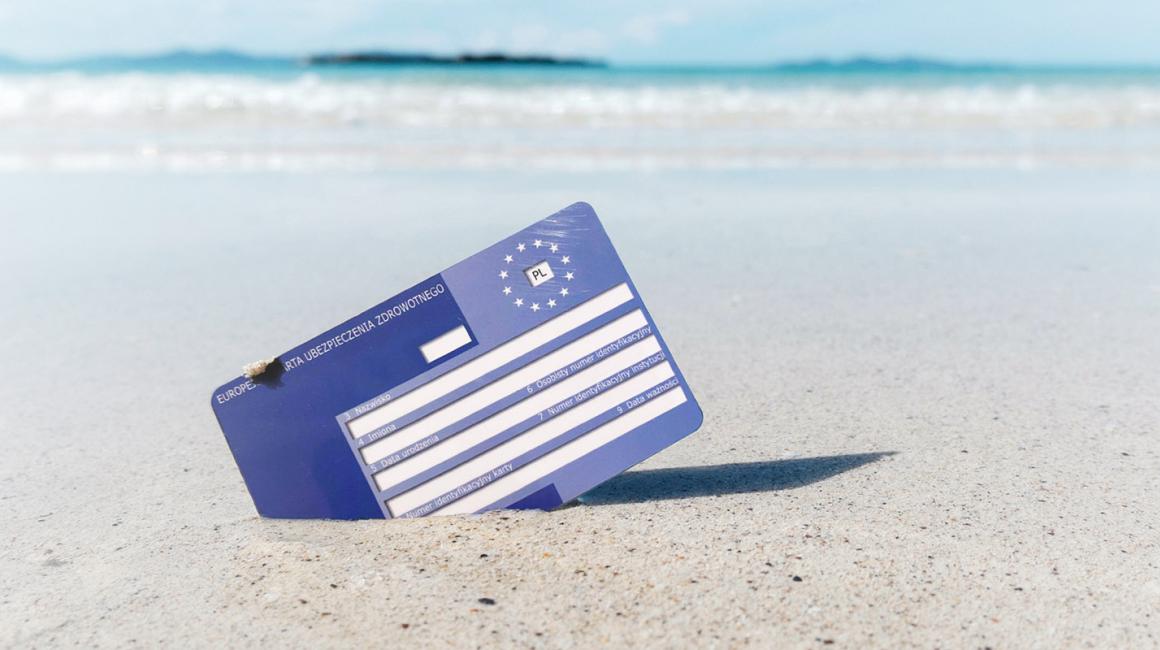 Karta EKUZ wbita w piasek na plaży. W tle błękitne morze.