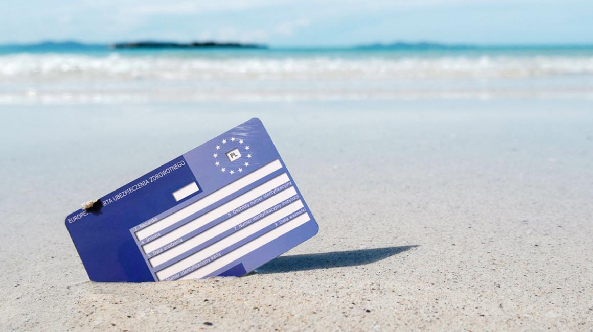 Karta EKUZ wbita w piasek na plaży. W tle błękitne morze.