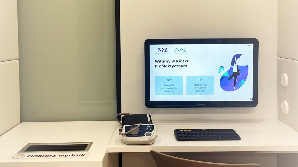 Widok wnętrza kiosku profilaktycznego. Ekran z powitanniem, klawiatura i ciśnieniomierz.