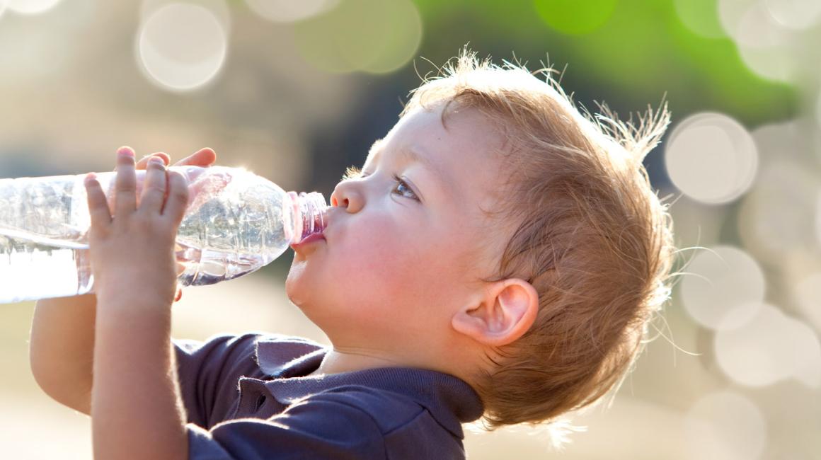 Kilkuletni chłopiec w upalny dzień pije wodę z buletki.