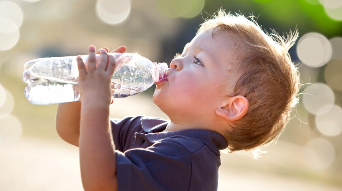 Kilkuletni chłopiec w upalny dzień pije wodę z buletki.