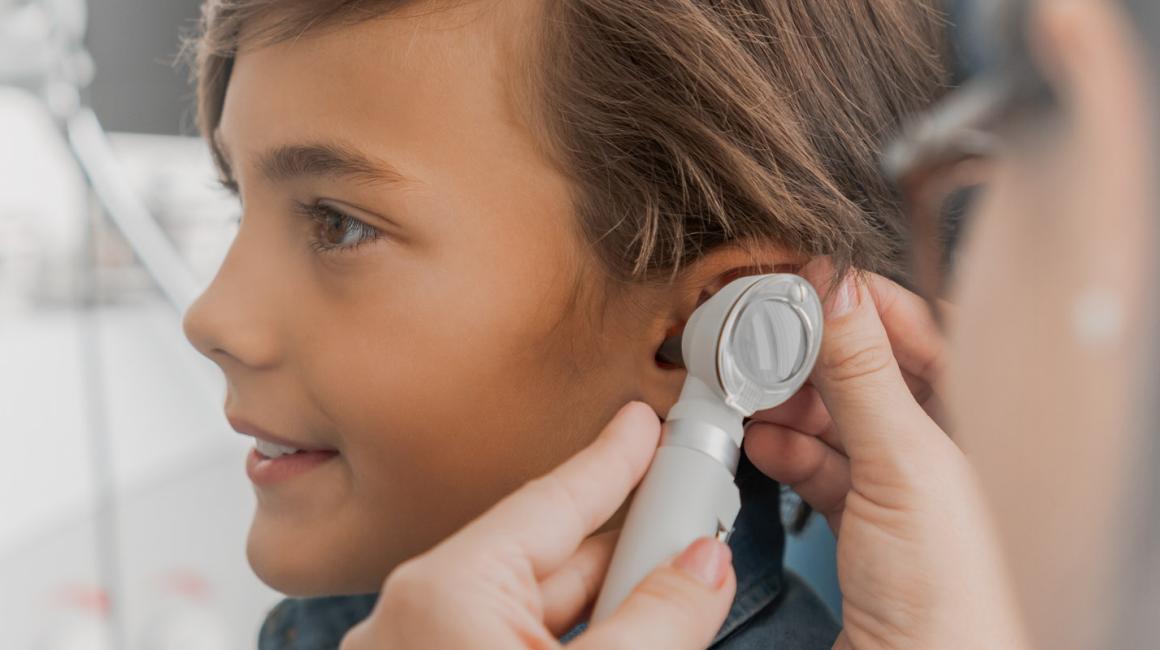 Chłopiec podczas wizyty u laryngologa. Lekarka bada mu ucho otoskopem.