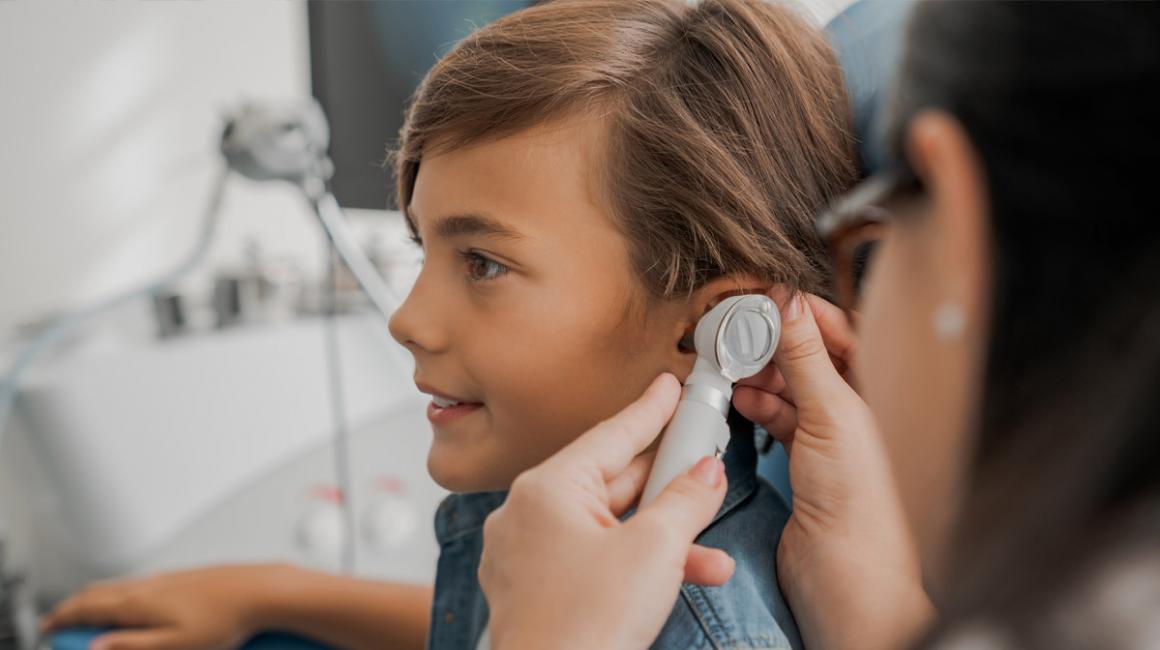 Chłopiec podczas wizyty u laryngologa. Lekarka bada mu ucho otoskopem.