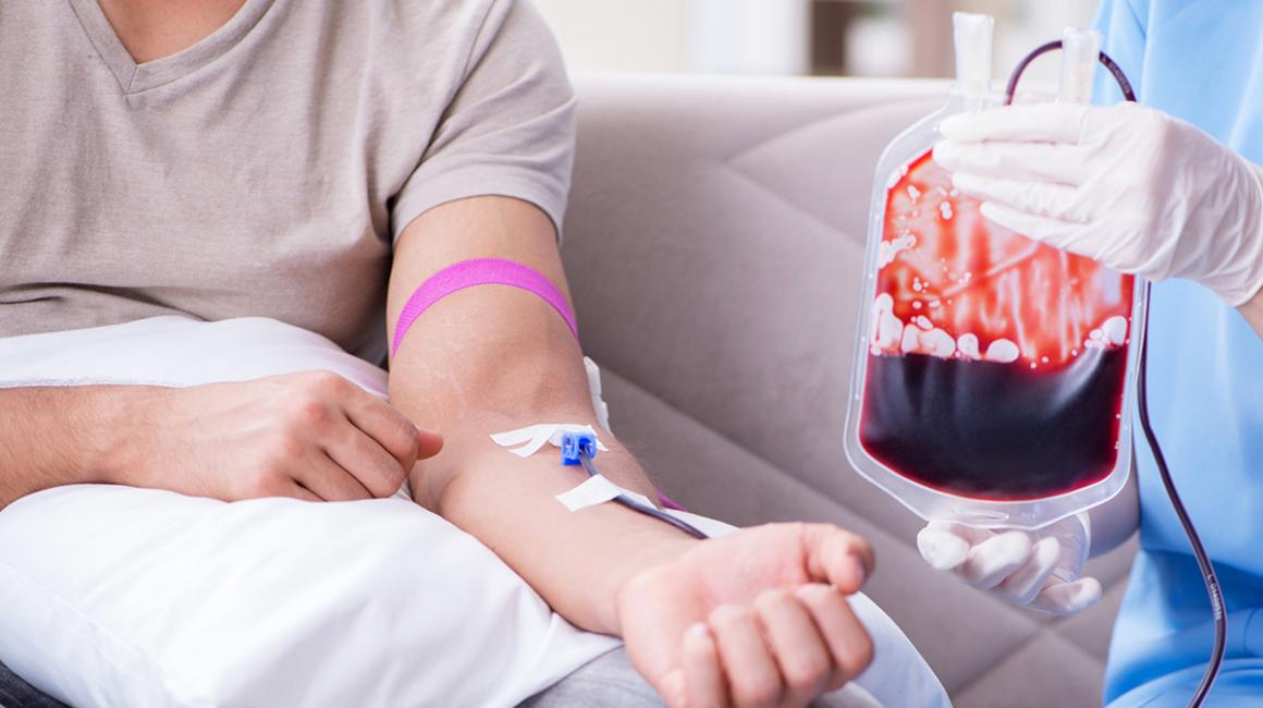 Osoba oddająca krew, z igłą w żyle i krwią spływającą do worka z krwią trzymanego przez personel medyczny. Widoczny tylko tułów osób.