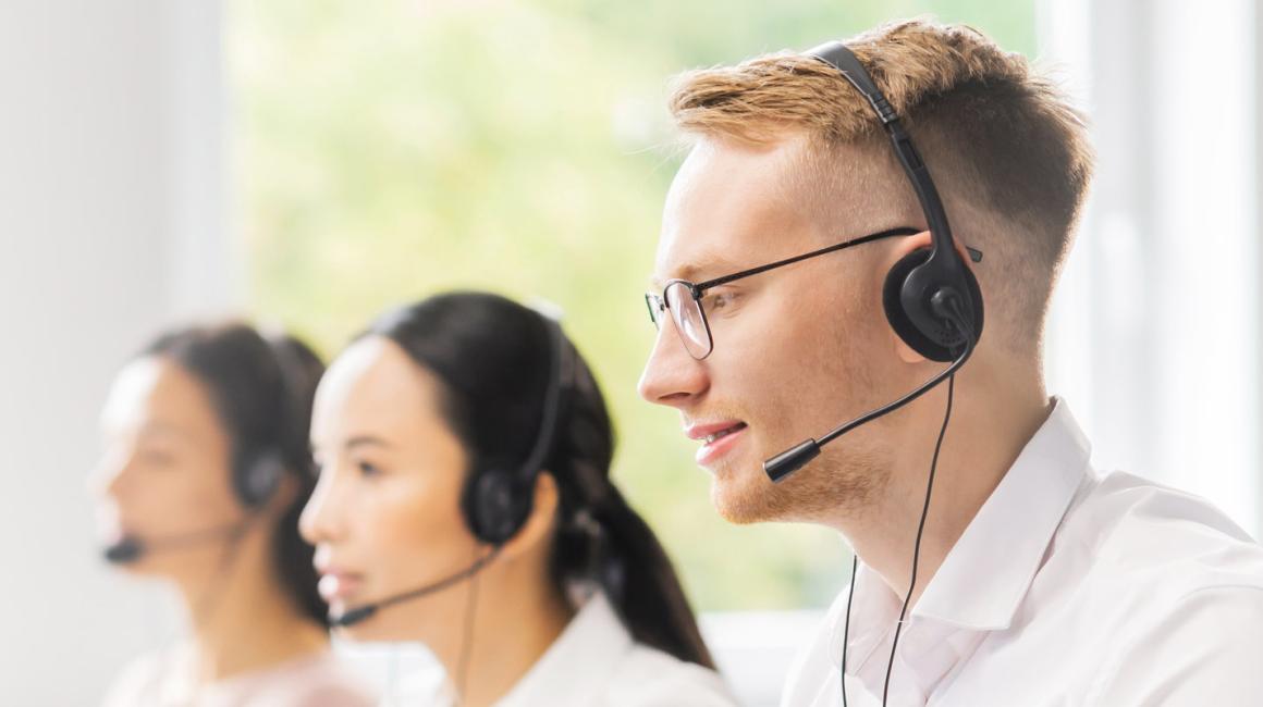 3 konsultantów w słuchawkach na uszach, siedzą przed ekranami komputera. Ujęcie z profilu, od pasa w górę. 