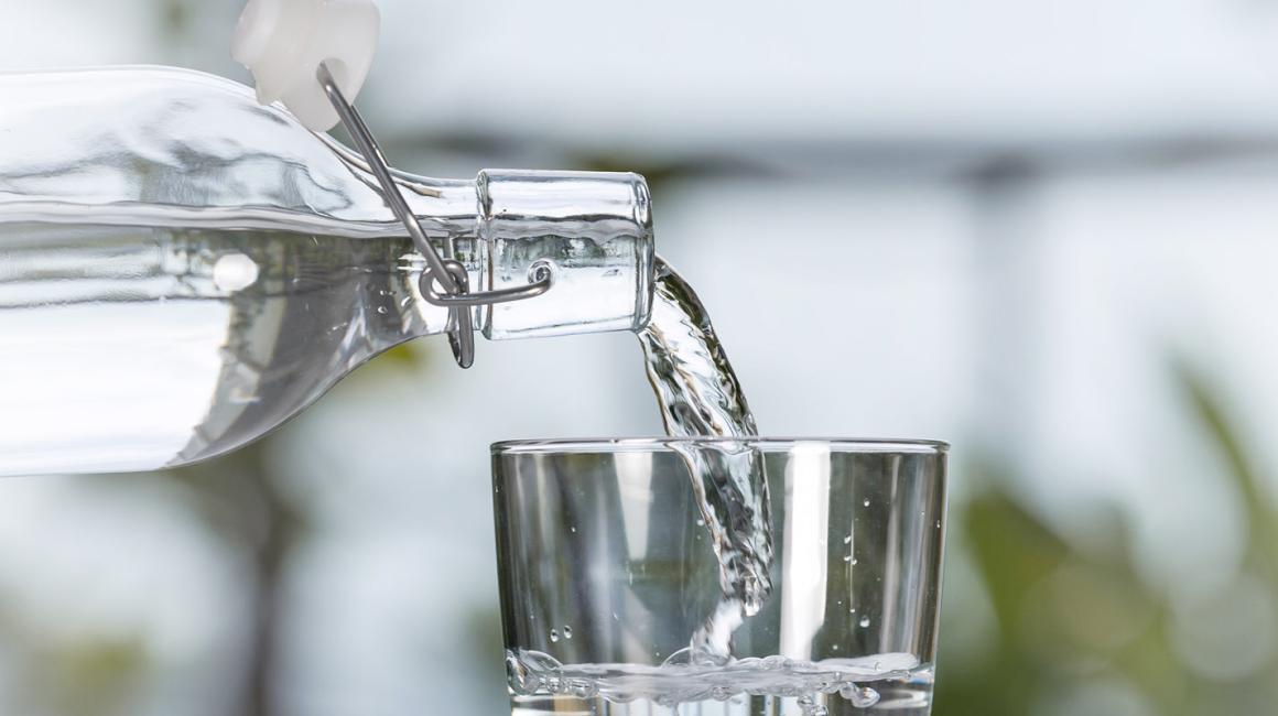 Szklanka, do której płynie woda z przechylonej butelki.