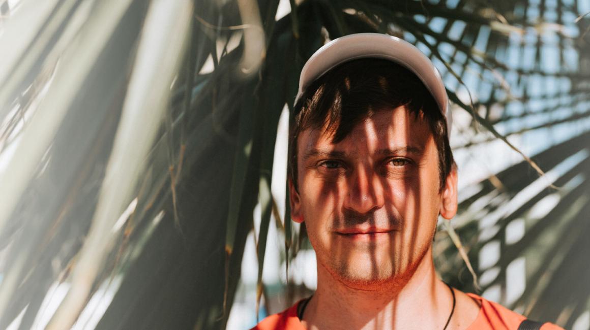 Mężczyzna w czpace z daszkiem w cieniu rzucanym przez liście palmy. Widok twarzy i liści.