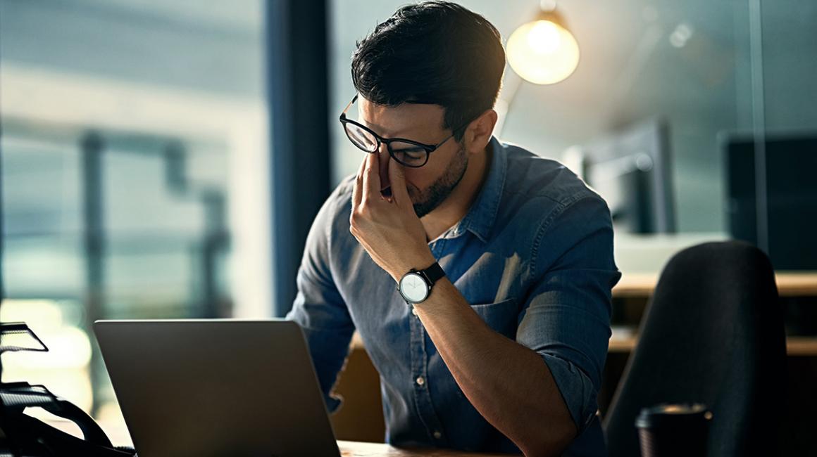 Mężczyna siedzi przed komputerem. Przeciera oczy ze zmęczenia.