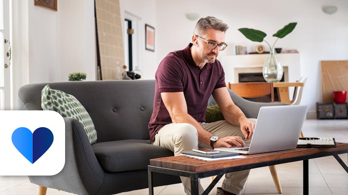 mężczyzna pisze coś w komputerze stojacym na "jamniku" przy kanapie 