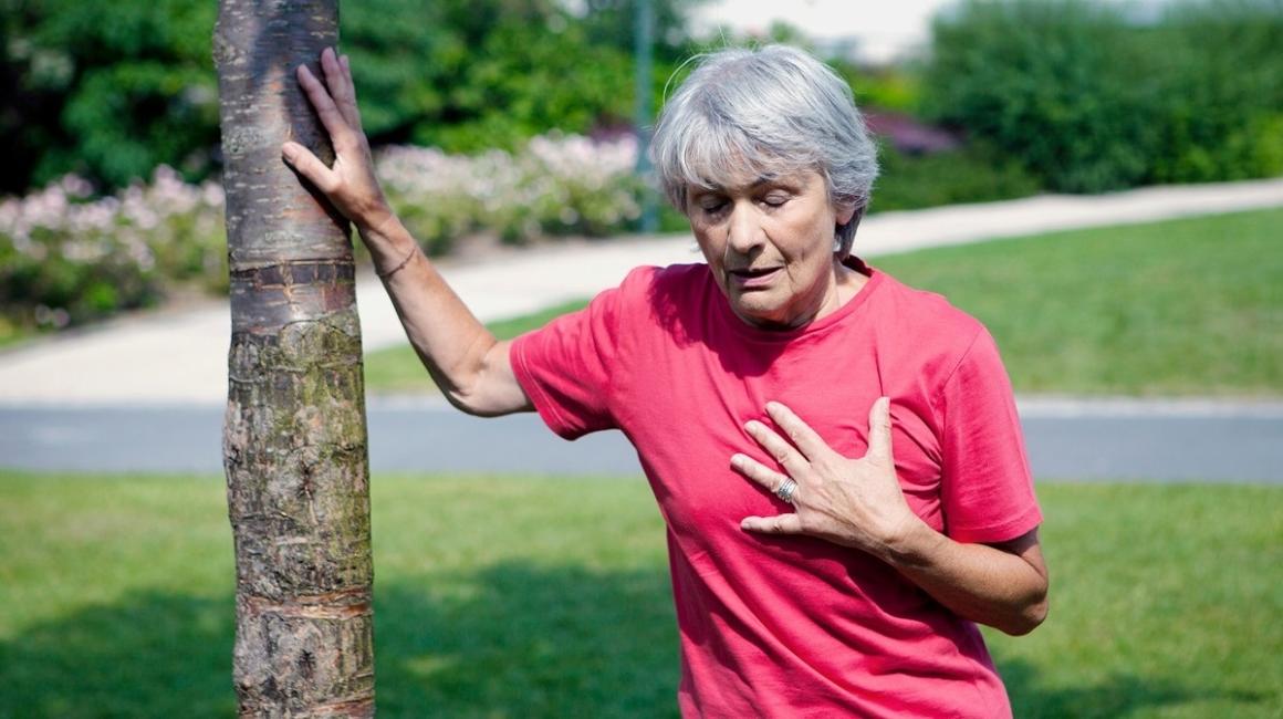 Kobieta trzymająca się ręką za serce, a drugą wspierająca się o drzewo
