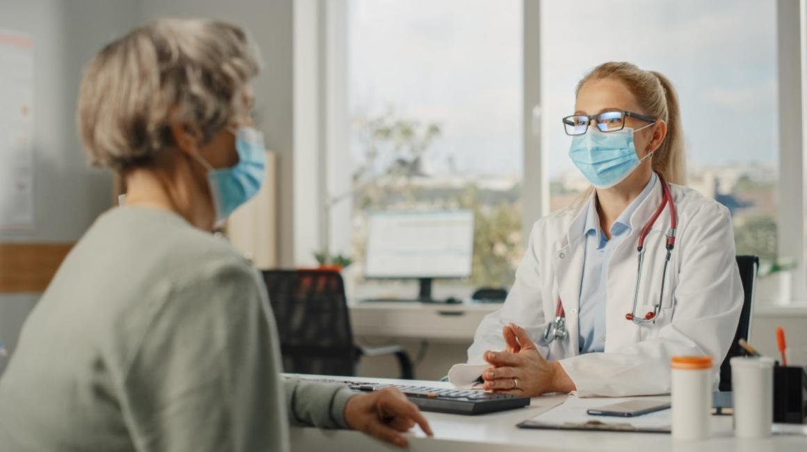 Starsza pani siedzi naprzeciwko lekarki w gabinecie. Ujęcie z boku.