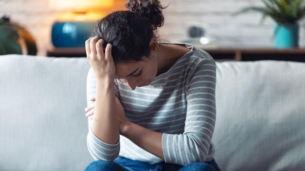 Kobieta na kanapie, głowa smutno zwieszona, podparta