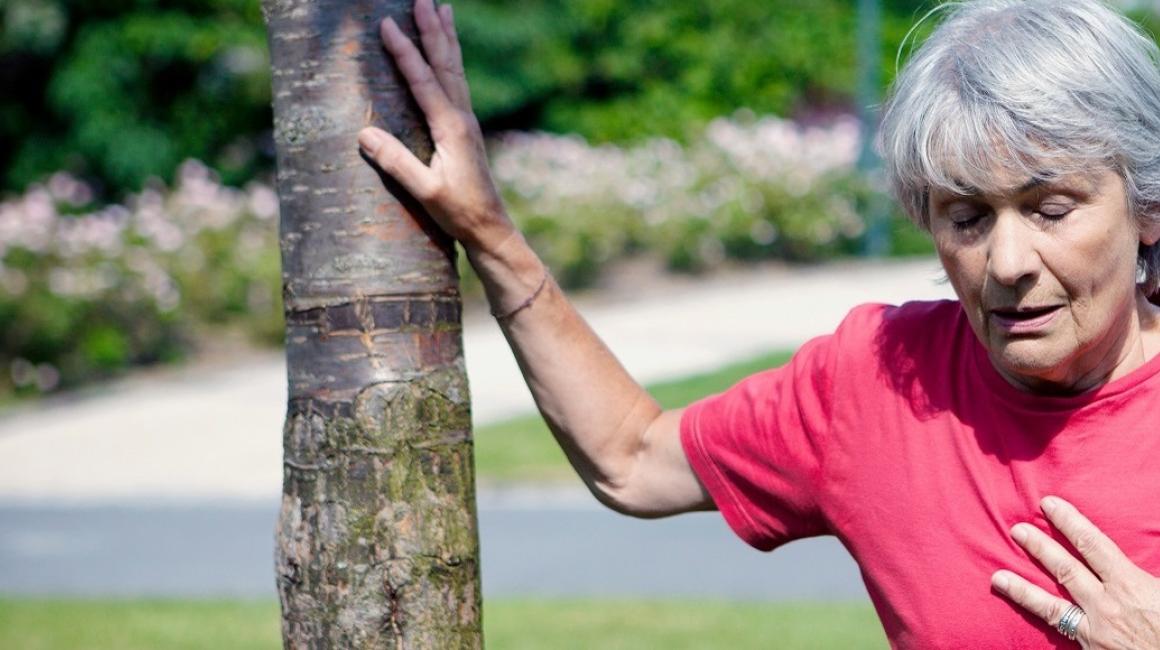 Kobieta trzymająca się ręką za serce, a drugą wspierająca się o drzewo