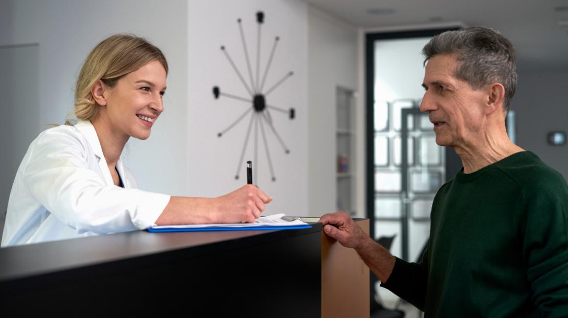 Starszy mężczyzna rozmawia z recepcjonistką w przychodni.