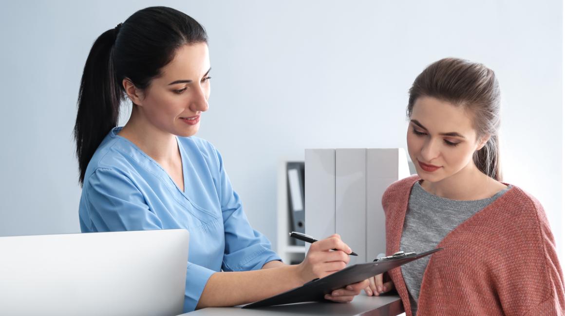 Małoda dziewczyna w przychodni rozmawia z recepcjonistką. 