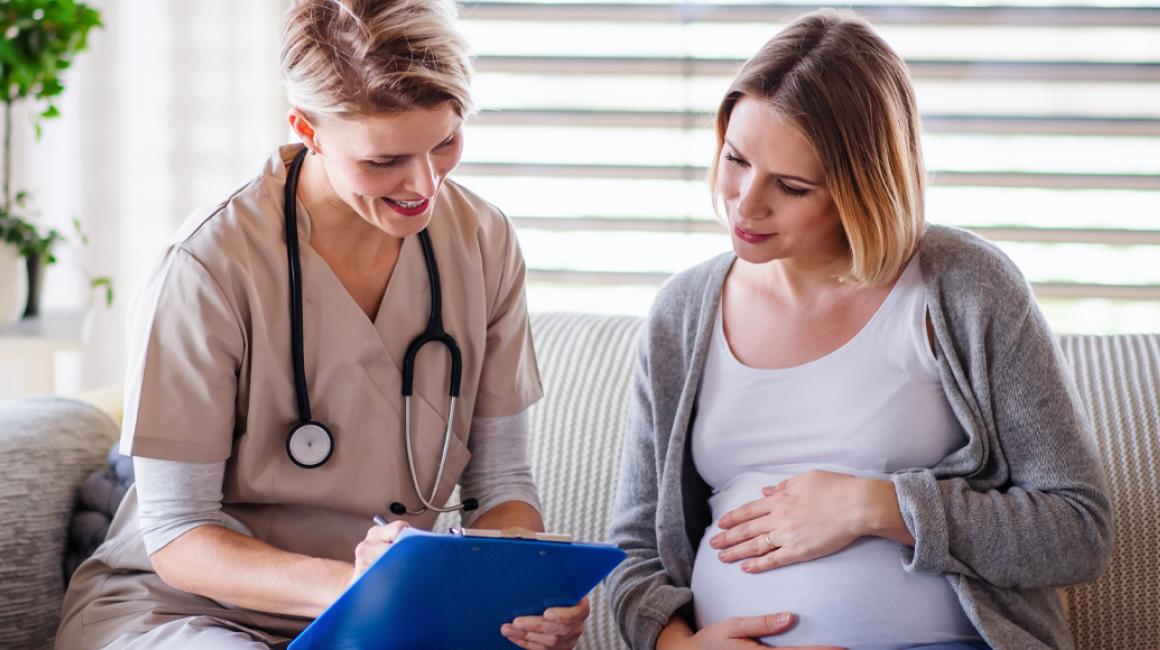 Położna podczas wizyty domowej u pacjentki w zaawansowanej ciąży. Omawiają wyniki badań.